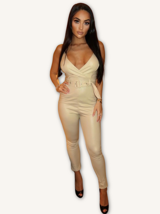 Model wears a beige faux leather jumpsuit with belted waist and plunging neckline. Model stands with one hand on her hip and the other on her thigh.
