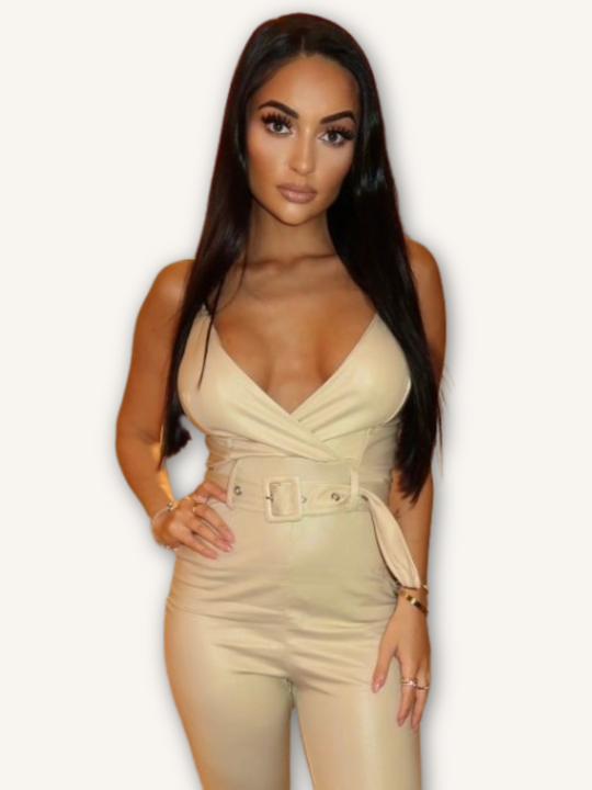 Model wears a beige faux leather jumpsuit with belted waist and plunging neckline.  Model faces the camera with one hand on her thigh and the other on her hip.