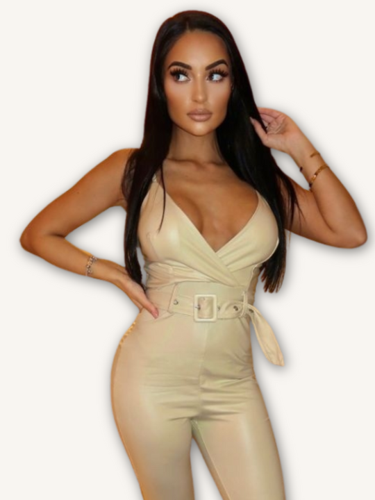 Model wears a beige faux leather jumpsuit with belted waist and plunging neckline. Model looks to the side, placing one hand on her hip and the other in her hair.