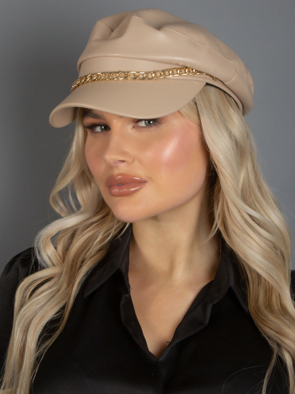 Model wears a beige pu leather paper boy hat with gold chain. The model  turns her head to the side, the side of the cap can be seen, imcluding the gold chain linked detailing.