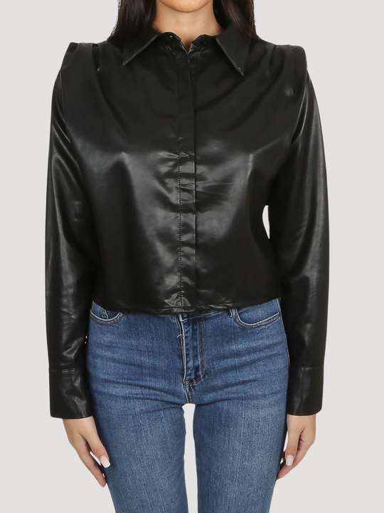 Model wears black faux leather shirt with pleated shoulders and long sleeve. The pu cropped front button shirt and collard neck. Closeup of the front of the shirt is visible, model stands with both hands at her sides.