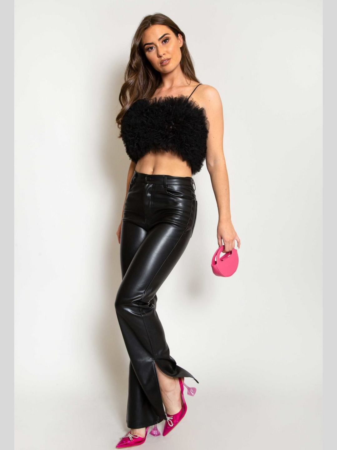 Full length. Model wears  a black organza ruffled crop top ,with spaghetti strap and zip back fastening. Model has tanned skin and long brown hair. Model wears the organza top, pu leather trousers and pink heeled shoes and mini bag.