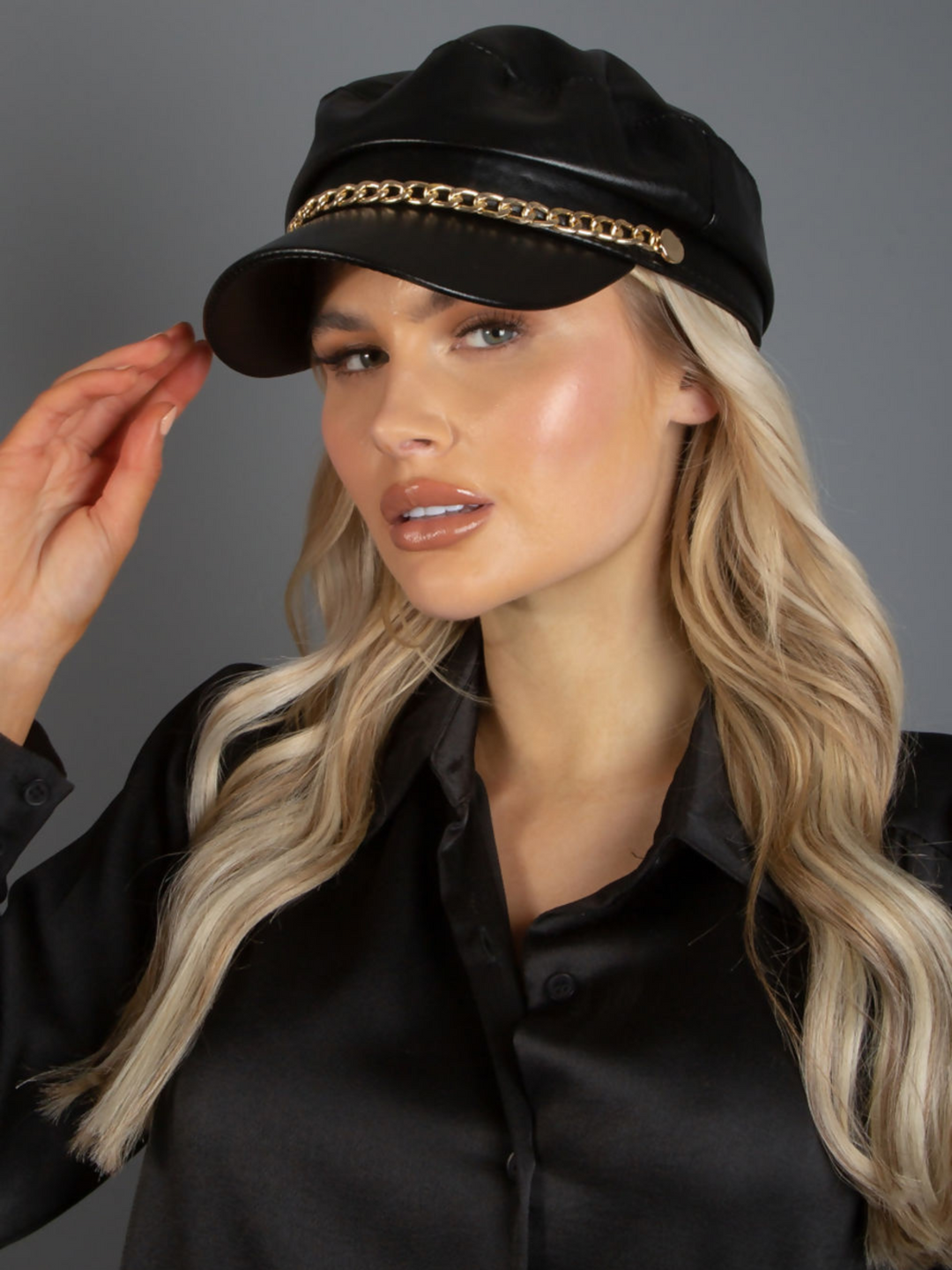 Mid length shot. Model wears a faux leather baker boy hat with gold chain detailing at the front.