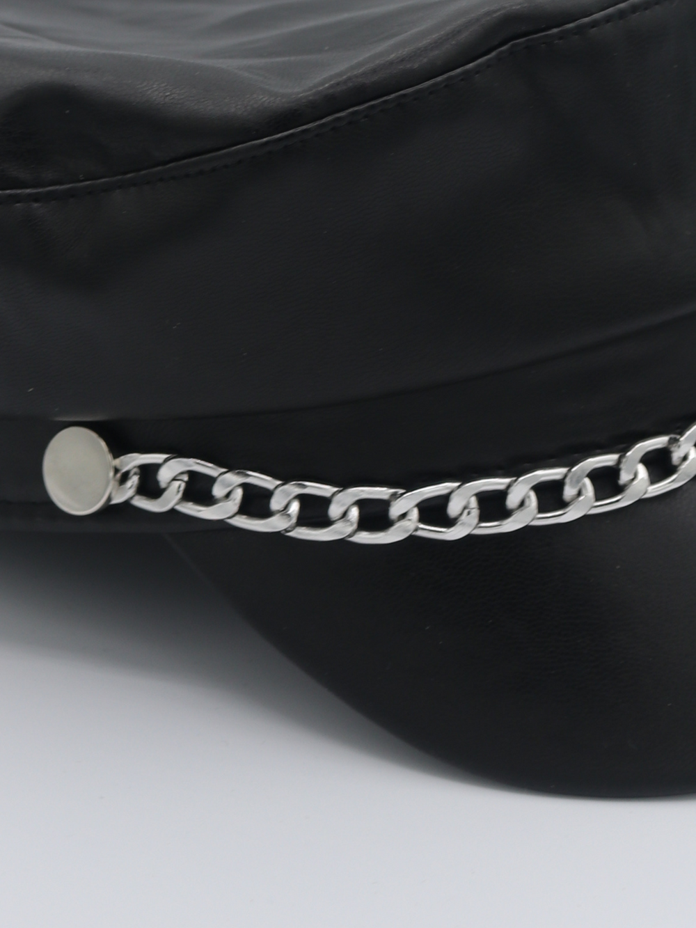 Close up of the pu leather hat. The picture shows a close up of the silver chain detailing at the front of the leather look PU baker boy hat.