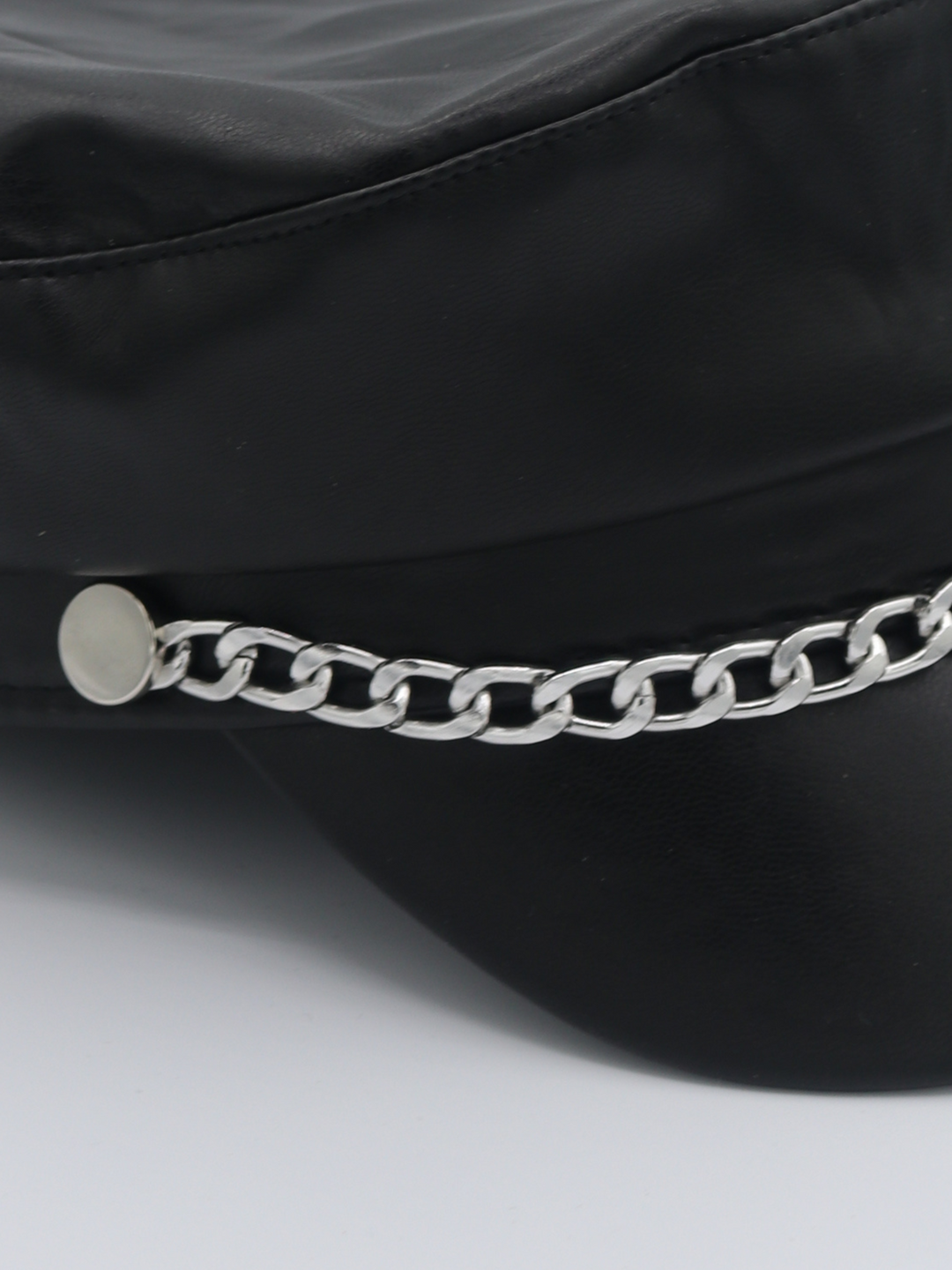 Close up of the pu leather hat. The picture shows a close up of the silver chain detailing at the front of the leather look PU baker boy hat.