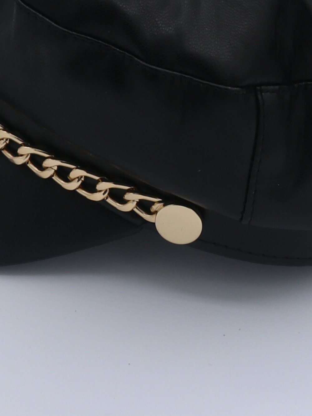 Close up of the cap, showing the gold chain. The cap is a leather look pu leather baker boy hat with gold chain detailing at the front.