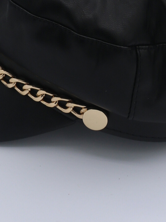 Close up of the cap, showing the gold chain. The cap is a leather look pu leather baker boy hat with gold chain detailing at the front.