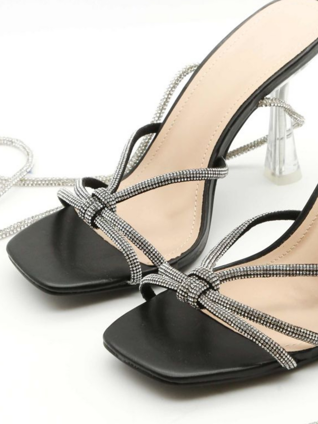 Product close up shot. The shoe is a  black patentt leather look muled shoe, with open toes and silver diamante cross over straps. The shoe also has a silver diamante strap that  fis designed to fasten along the shin.