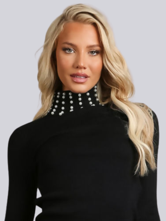Female model wears a black knitted turtle neck jumper, with pearl  detailed pearl accents at the high neck and  cuff. The female model has tanned skin and long blonde hair, the top of the jumper can be seen, including the pearl detailing at the turtle neck.