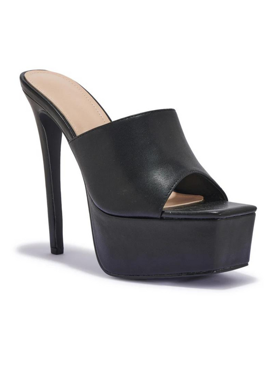 Black heeled mules that have a thick platform base and stiletto shoes. The picture shows the shoe at a 120 degree angle. The side of the shoe and the tall stileto shoe can be seen.