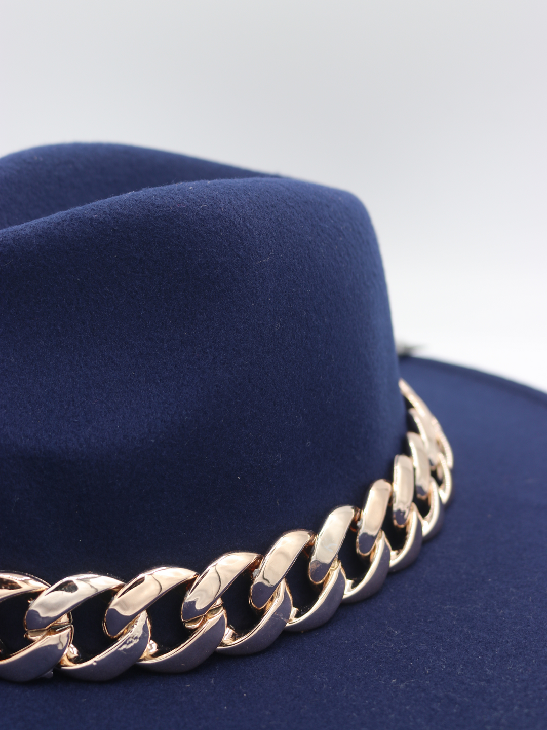 The side of the navy blue felt fedora hat can be seen. The chunky gold linked chain is also visible.
