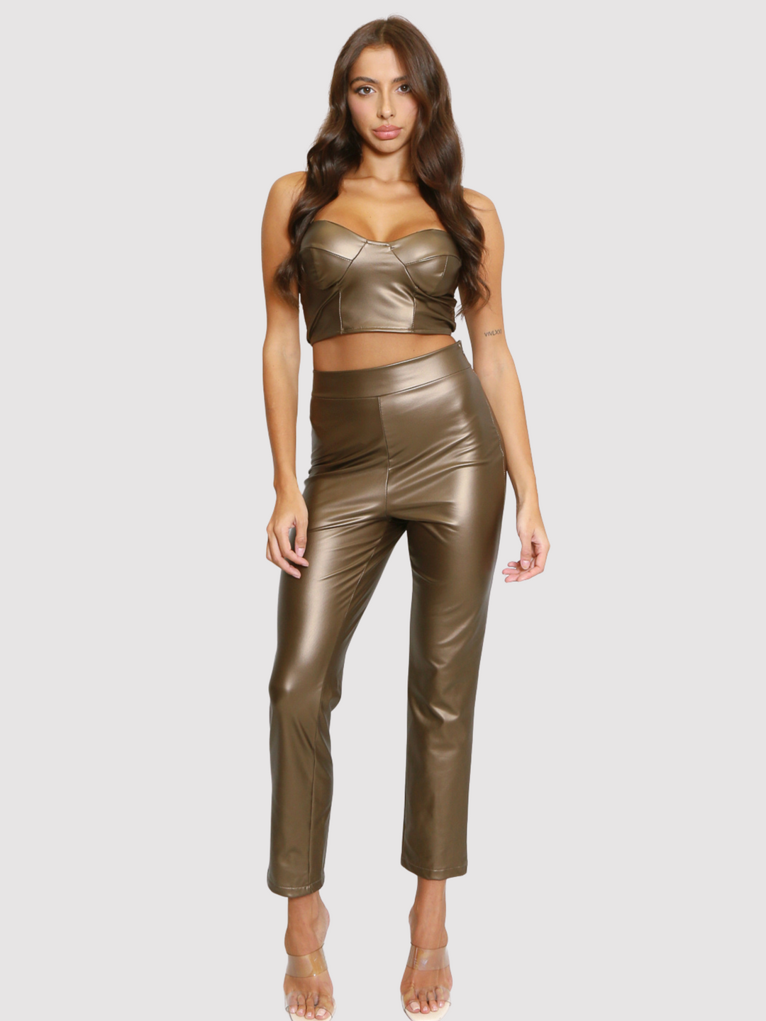 Female model stands before a plain background. The female model wears  a brown pu faux leather crop top and trouser sets. The crop top has a sweet heart neckline and a concealed side zip fastening. The model has tanned skin and long brown hair, she faces the camera and has her hands by her sides.