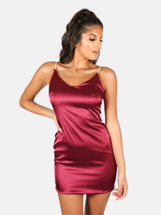 Model wears a red wine coloured satin mini dress with diamante straps and concealed zip back fastening. Model stands with one hand on her hip and the other by her side. The front of the dress can be seen.