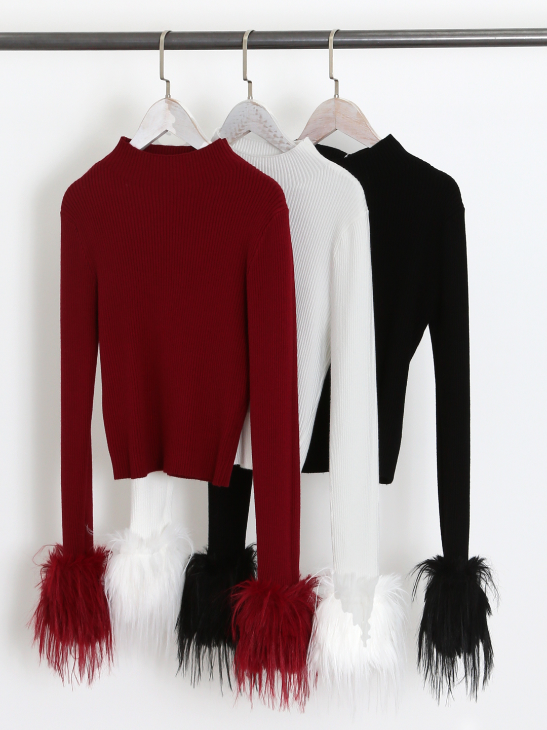 Clothing rail shows 3 long sleeve fine knit jumpers, with a crew neckline and faux fur cuffs. The jumper colours are red, white and black, each jumper shows the faux fur cuffs.