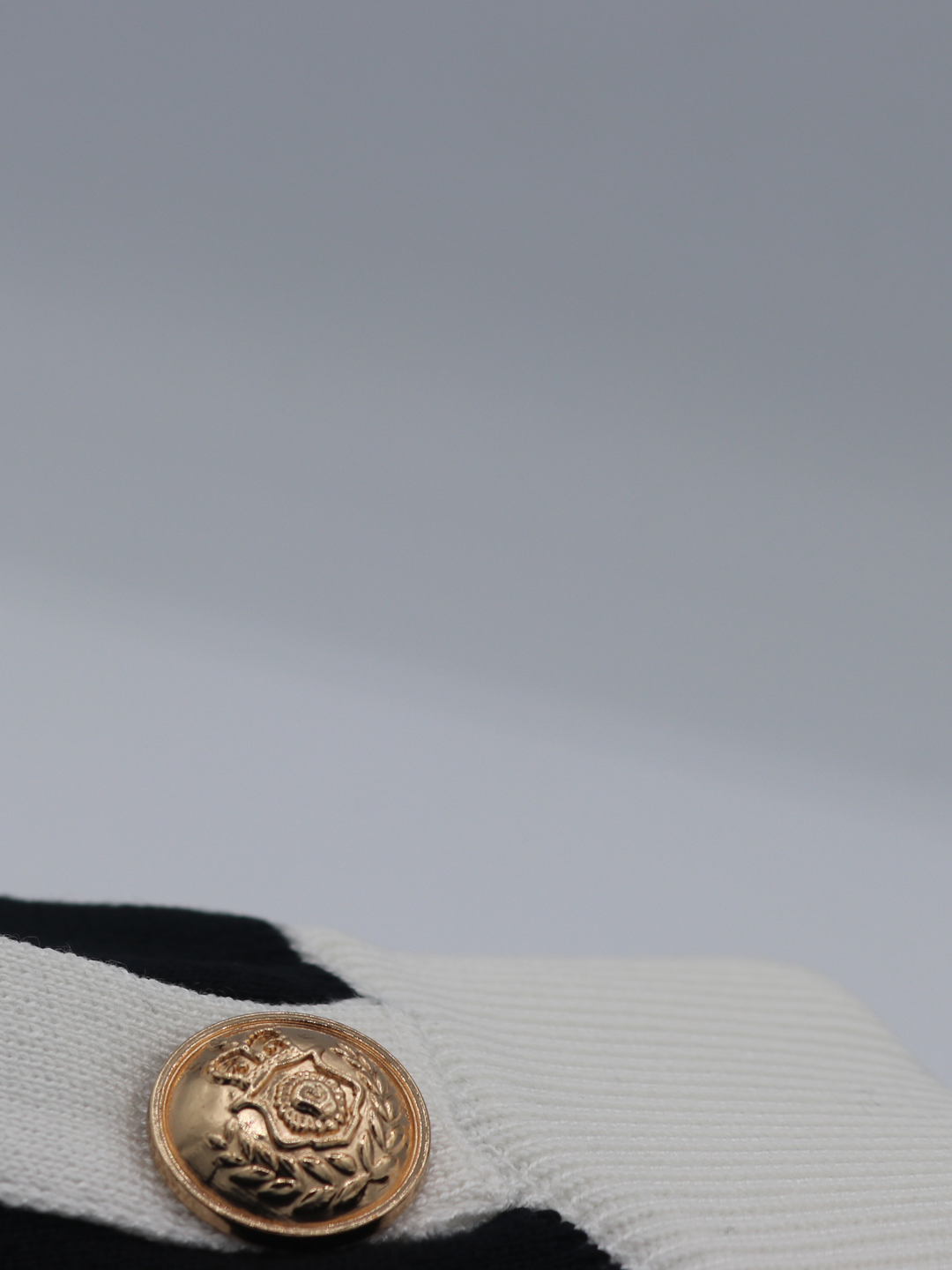 Close of gold military buttons on a black and white fine knit shorts set; with matching black and white crop top and and shorts and gold military buttons. One miltary button is visible.