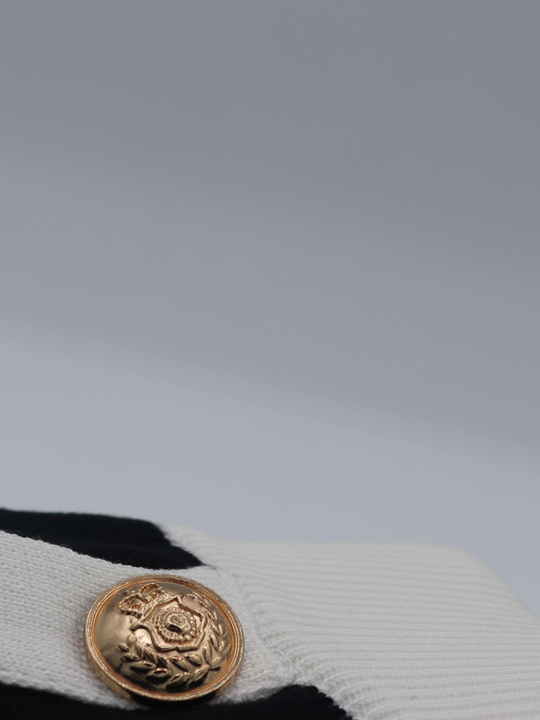 Close of gold military buttons on a black and white fine knit shorts set; with matching black and white crop top and and shorts and gold military buttons. One miltary button is visible.