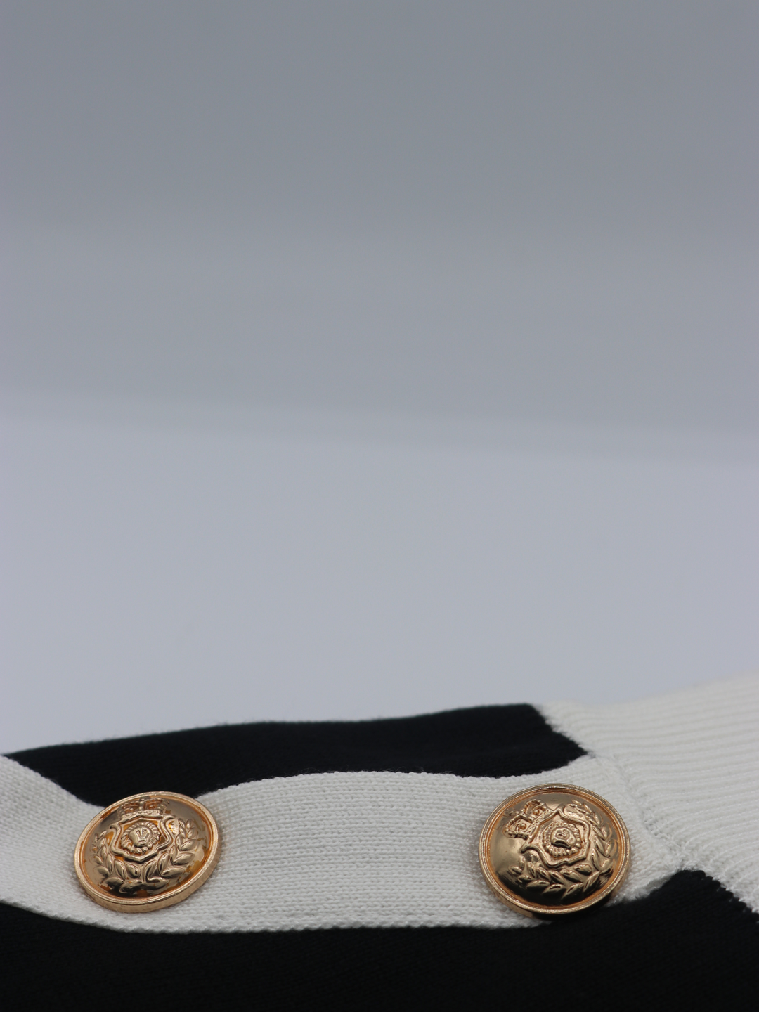 Close of gold military buttons on a black and white fine knit shorts set; with matching black and white crop top and and shorts and gold military buttons. Two miltary button is visible.