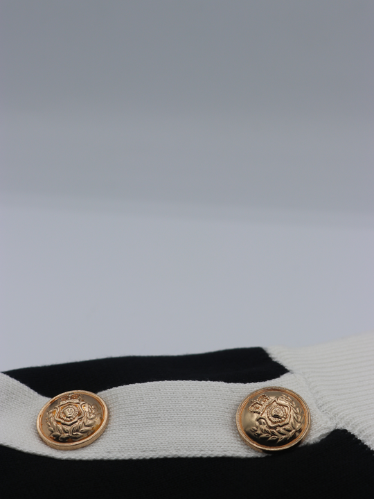 Close of gold military buttons on a black and white fine knit shorts set; with matching black and white crop top and and shorts and gold military buttons. Two miltary button is visible.
