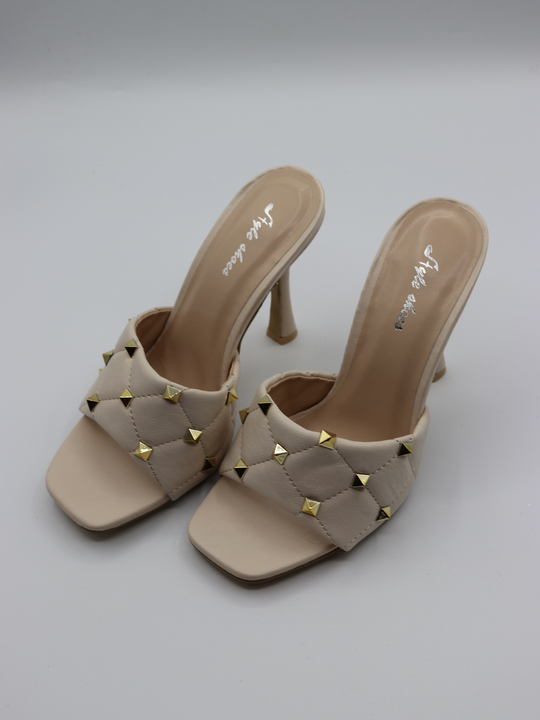 Cream quilted faux leather mule heels with gold studded heels. The studded pair of heels is at a slight diagnal angle.