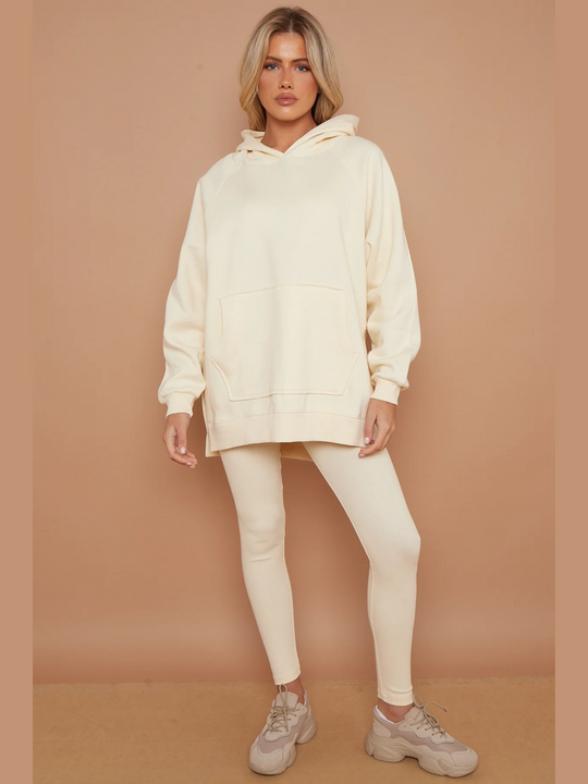 Full length shot. Model wears oversized cream hoodie with matching ribbed leggings.  Model faces forward, placing one leg to the side and her hands by her side. Model wears a chunky trainer shoe.
