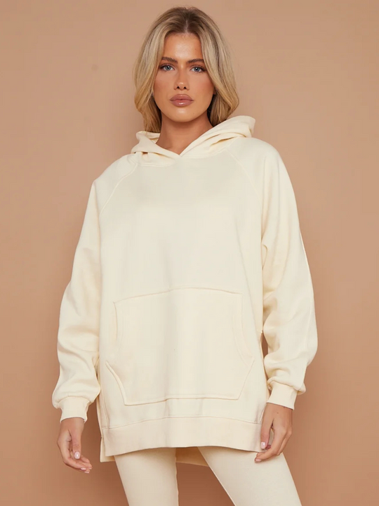 Model wears oversized cream hoodie with matching ribbed leggings. Model has blonde hair, she faces the camera, places both hands by her side.