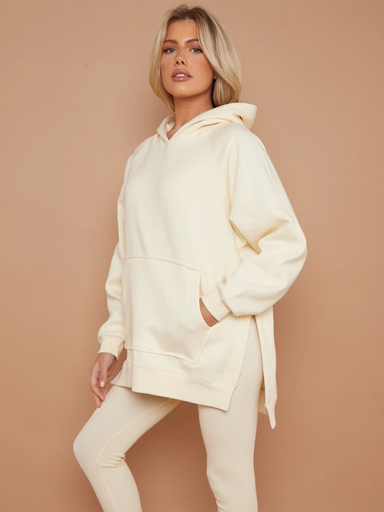 Model wears oversized cream hoodie with matching ribbed leggings.  Model stands to the side and places one hand in her pocket and the other by her side.