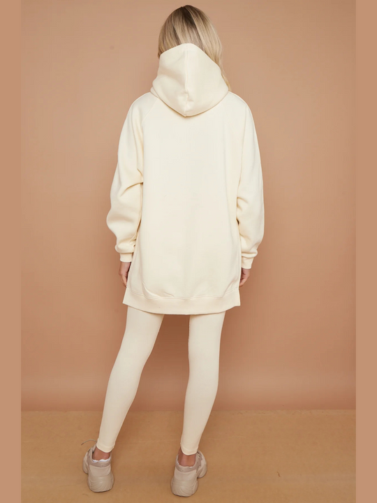Full length shot. Model wears oversized cream hoodie with matching ribbed leggings. She stands with her back to the amers, the oversized hoodie can be seen and the ribbed leggings. The model wears chunky cream trainers.