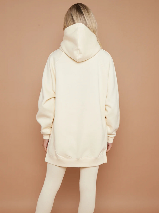 Model wears oversized cream hoodie with matching ribbed leggings. Model stands with her back to the camera, she places oth arms by her side.