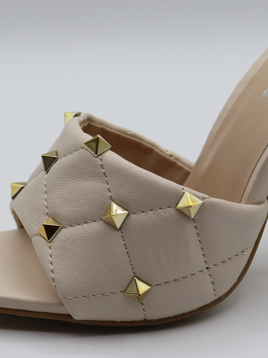 Cream quilted faux leather mule heels with gold studded heels. Closeup of  quilted shoe with gold studded detailing.