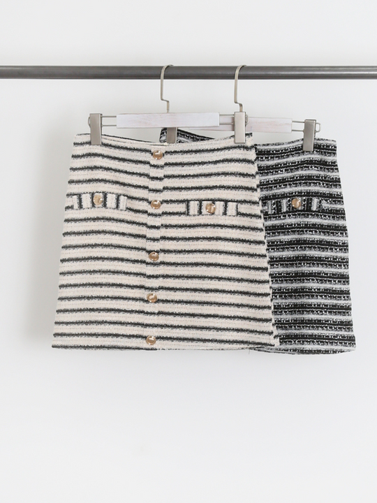 Tweed mini skirts with gold military buttons hanging on a clothing rail.