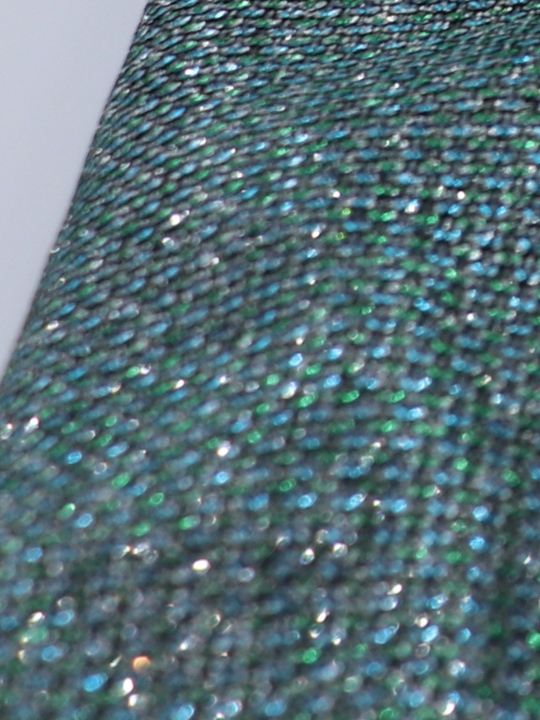 Closeup of green glitter micro mini dress with long sleeves. A closeup of the glitter material can be seen.