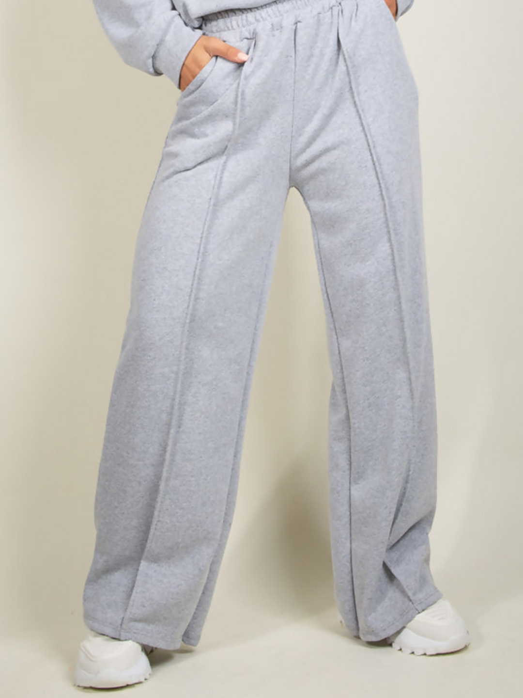 Model wears grey round neck long sleeve jumper and elasticated wide leg matching joggers. The joggers has a pockets and decorative seam.  The wide leg jogger can be seen, model wears white trainers.