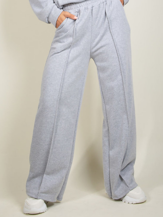 Model wears grey round neck long sleeve jumper and elasticated wide leg matching joggers. The joggers has a pockets and decorative seam.  The wide leg jogger can be seen, model wears white trainers.