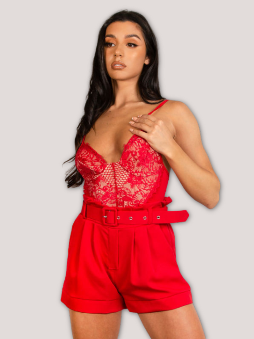 Model wears a red bodysuit with lace panel detailing. Model stands with one hand behind her back anf the other holding the tops spaghetti straps.