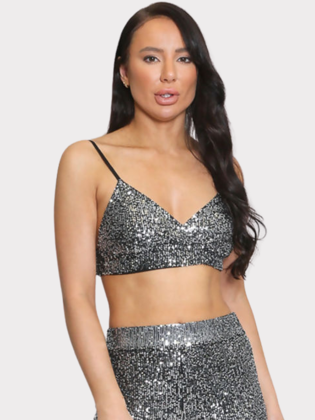 Mid Shot. Model wears silver sequin bralette with a v neck neck line and adjustable straps. The sequined matching trousers have an elasticated waist. Model faces the camera and has long brown hair.