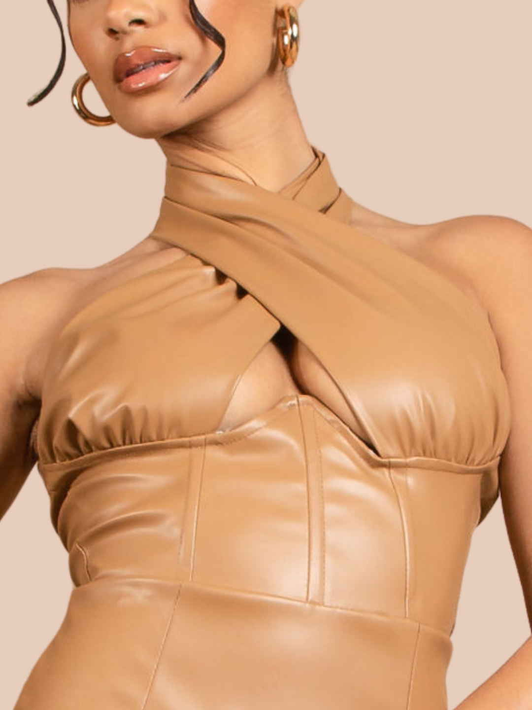 Model wears a faux leather tan coloured mini dress with cross over  halter neck design, panelled front, open back and back zip fastening. Closeup of the halter neck can be seen.