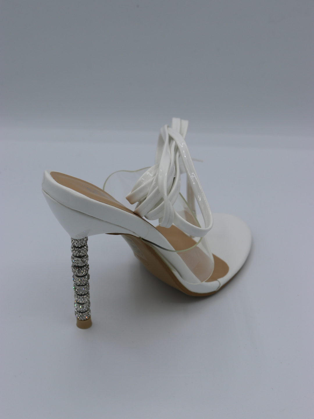 White strappy mules shoes with diamante stiletto heel. The perspex strap that goes across the shoe is visible, as is the white straps that can be used to go up the legs or around the ankles.