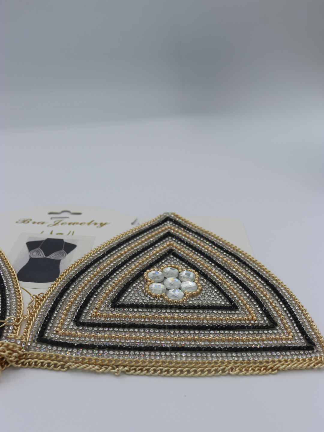 Close up of centre of the jeweled diamante bralette. The close up demonstrates the diamante and rhinestone design.  The gold chain fastening can be seen.  The packaging picture can be seen in the background.