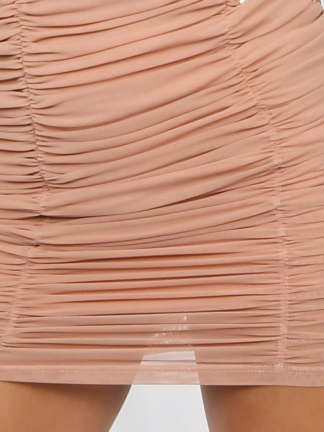 Extreme close up of skirt. Model wears a peach coloured ruched mini skirt tha has an elasticated waist.