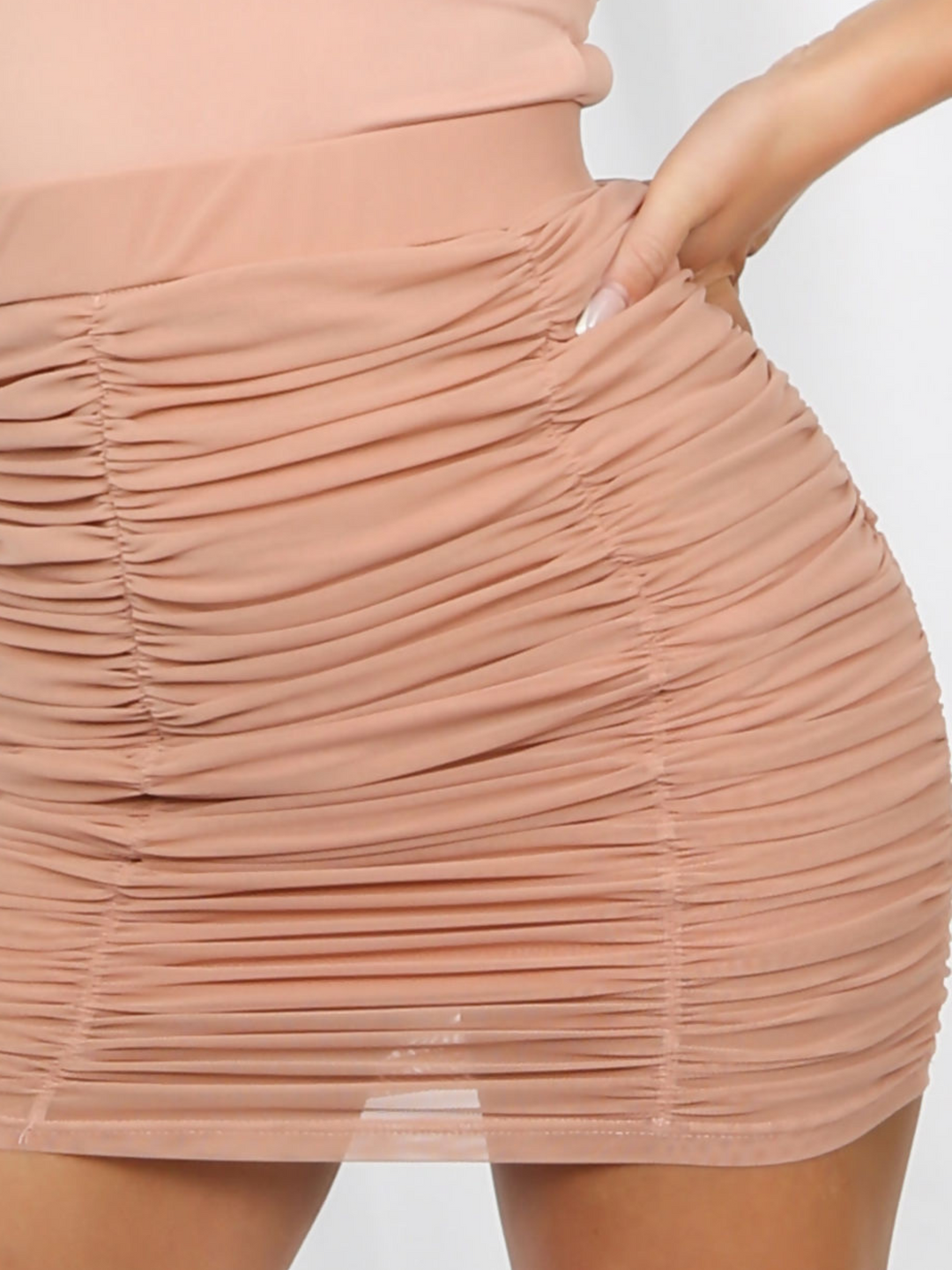 Close up of skirt. Model wears a peach coloured ruched mini skirt tha has an elasticated waist.