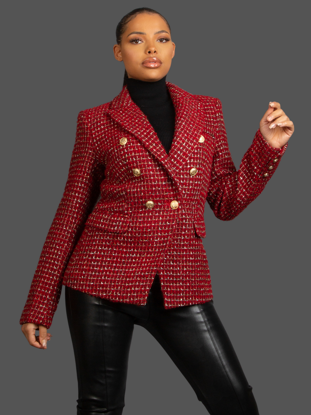 Model wears Red Wine Double Breasted Tweed Blazer, With Metallic Yarn Shimmer and Military Gold Buttons. The model as light brown skin and her hair pulled back into a ponytail. The model faces the camera, with the front of the blazer visible, including the gold button detailing. Model places one hand by her side and the other slightly bent, the military  gold button design of located on the  cuffs of the sleeves can be seen.