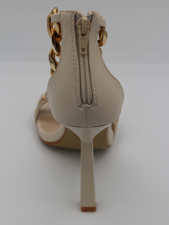 A cream shoe with gold detail at the base strap as well as gold chain detailing at the ankle. The photograph shows a close up of the back of the shoe, showing the cream heel and zip to the back of the shoe, that closes and secures the shoe.
