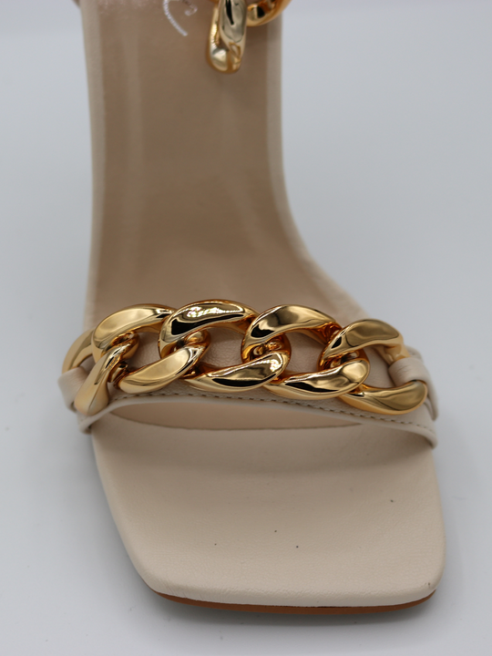 A close up of the mid position chunky gold detailing that goes across the cream strap. of the shoe.