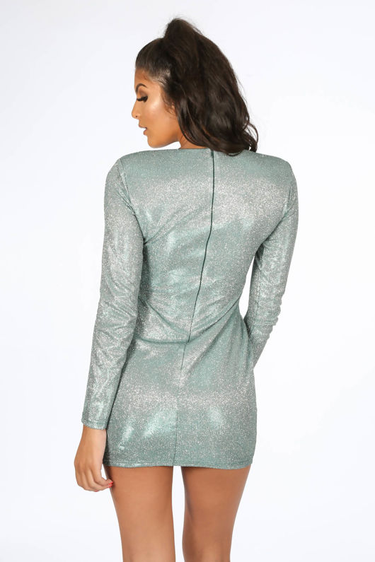 Model wears green glitter micro mini dress with long sleeves.  Model stands with her back to the camera. The back shows a concealed zip fastening.