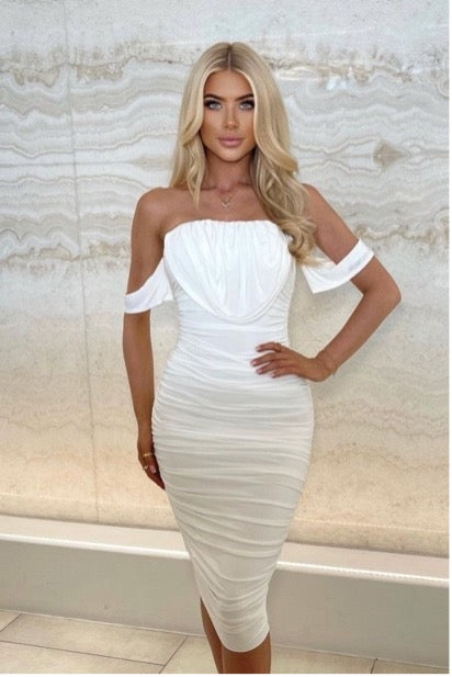 Model wears a double lined slinky white ruched midid dress with draping detailing at the torso. Model has her hands on her hips and steers directly into the camera.