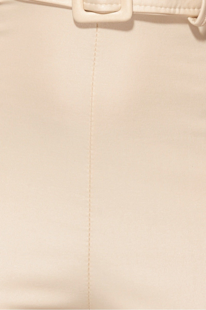 Model wears faux leather beige jumpsuit with high waisted belt . The jumpsuit has a skinny fit  style and a plunging neck line.  Close up of the faux leather material.