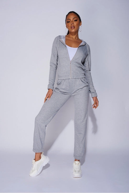 Model wears a light weight tracksuit with front zip fastening and draws string hood.  Model places one leg to the side and looks directly into the camera.