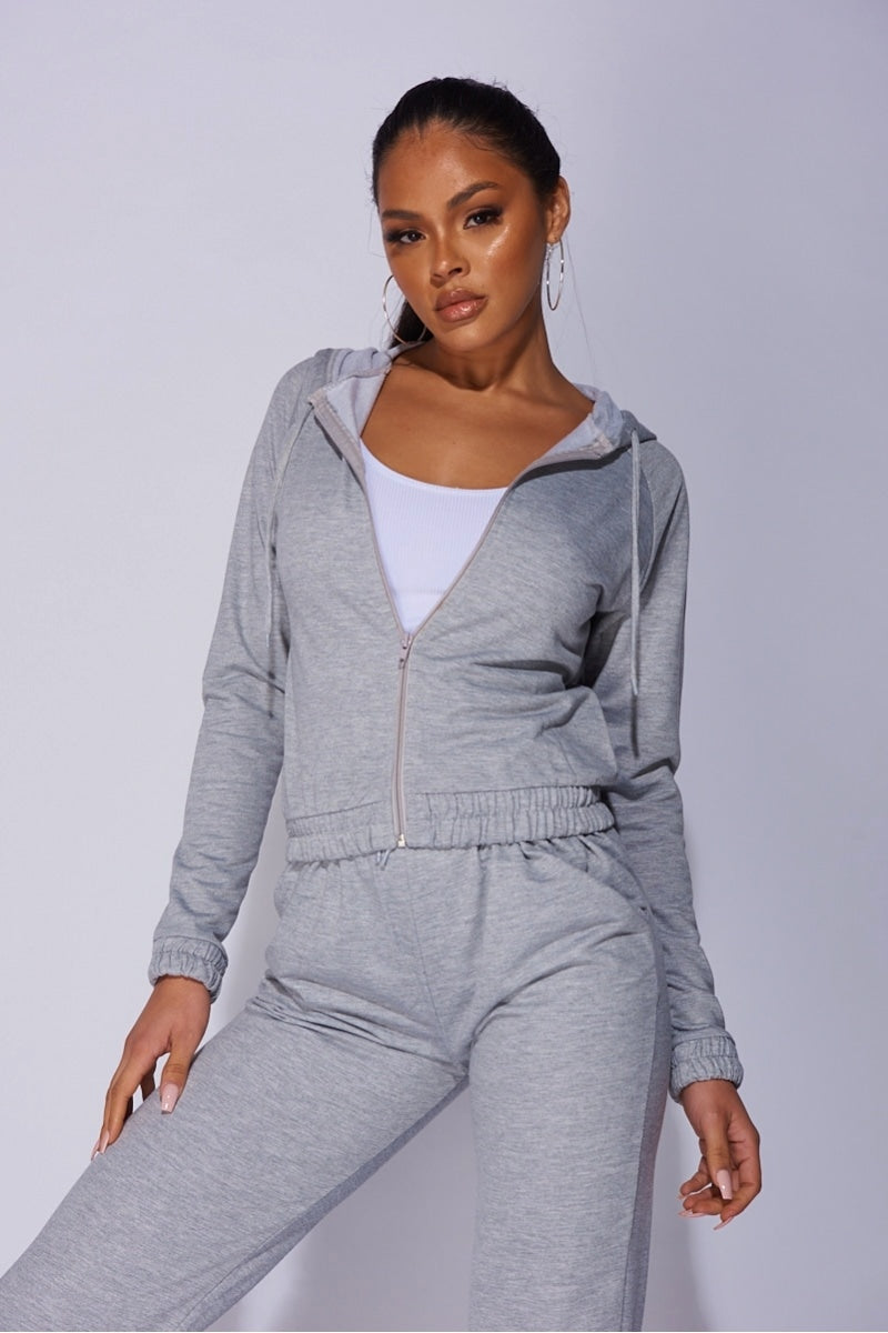 Model wears a light weight tracksuit with front zip fastening and draws string hood.  Model faces the camera with one leg to the side.