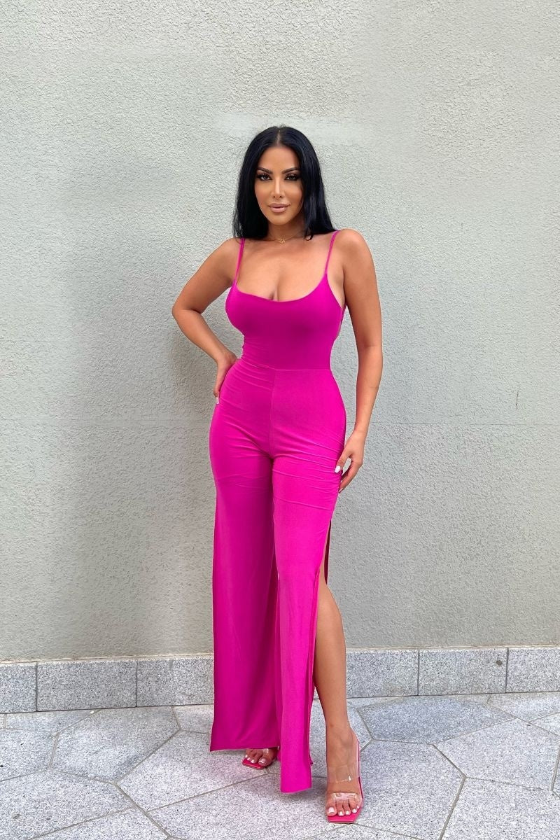 Model wears slinky magenta jumpsuit with a  scoop neck and spagehetti strap.  The jumpsuit  has thigh a thigh high split on each leg.  The jumpsuit has a low back and strap fastening.  Model faces the front and places one hand on her hip and the other by her side.