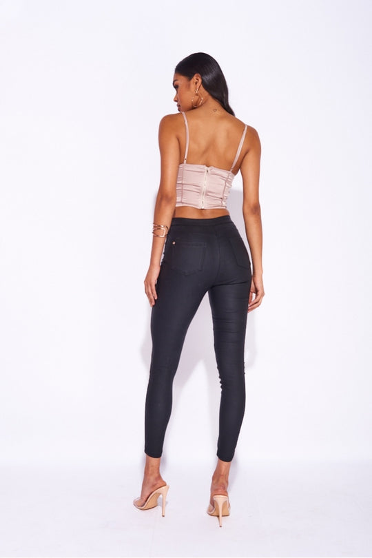 Model wears a mocha satin crop top, with bomne detailing and  a mocha lace trim. Model wears black trousers. Model stands with her back to the camera. The close zip fastening tp the top is visible.